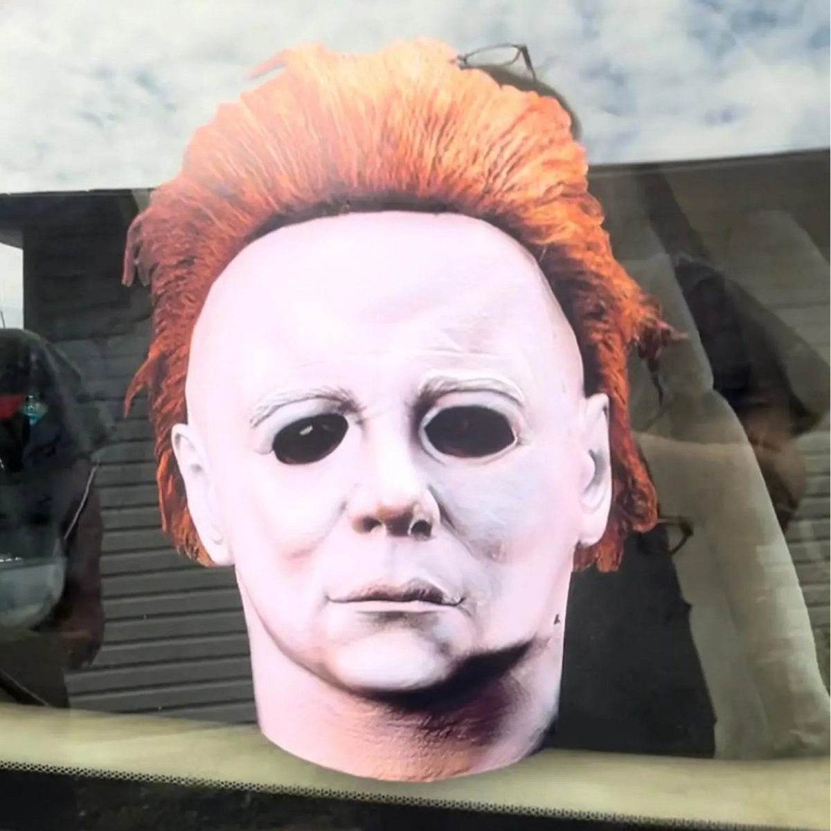 A large contour cut decal of Michael Myers mask shown resting on a car window.