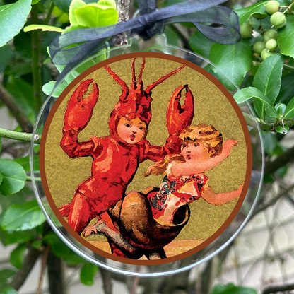 A round clear glass hanging ornament with a vintage-style illustration of a red lobster boy and an escargot girl, suspended by a dark ribbon against a background of green leaves and branches.