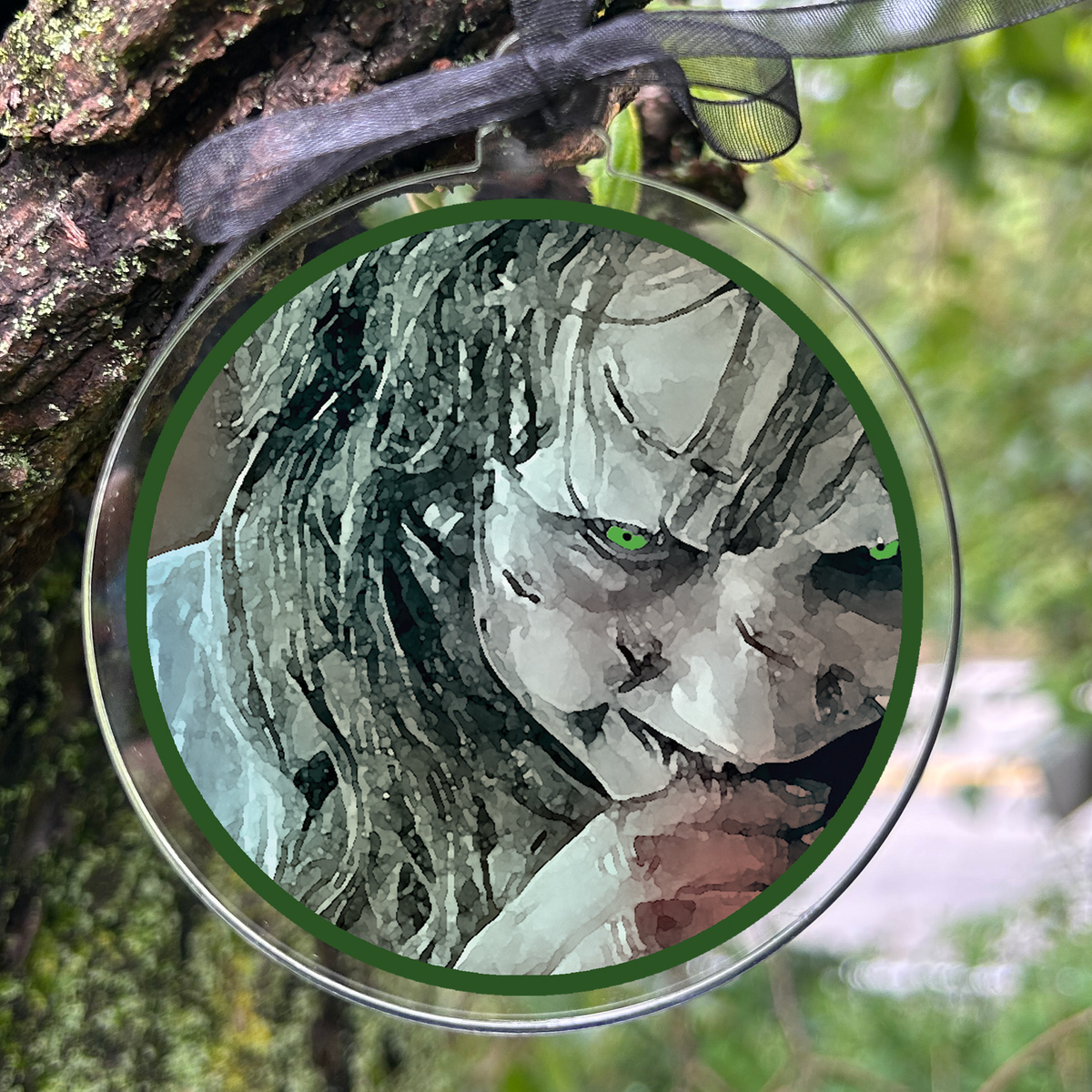 A round clear acrylic hanging ornament with a black ribbon, featuring Regan from the Exorcist, photographed hanging from a mossy tree branch 
