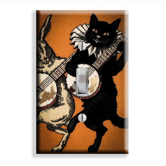 A rectangular light switch plate cover featuring a vintage-style illustration of a black cat and a beige rabbit playing banjos against an orange background, shown on a plain white backdrop.