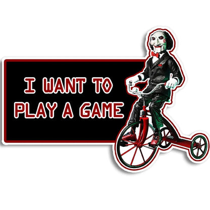A die-cut sticker featuring Jisaw Puzzle Billy riding a red tricycle next to a black rectangle with the text 'I WANT TO PLAY A GAME' in red outlined letters, shown on a white background.