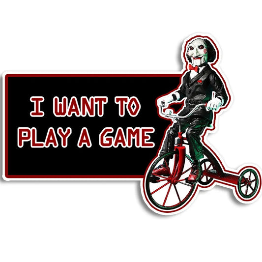 A die-cut sticker featuring Jisaw Puzzle Billy riding a red tricycle next to a black rectangle with the text 'I WANT TO PLAY A GAME' in red outlined letters, shown on a white background.